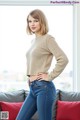 A woman in jeans and a sweater posing on a couch.