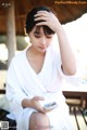 A woman in a white robe sitting on a bench looking at her phone.