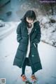 A woman standing in the snow wearing a long black coat.