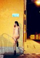 A naked woman standing in front of a yellow wall.