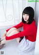 A woman in a red sweater and white skirt sitting on the floor.