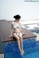 A woman in a white bikini sitting on the edge of a pool.