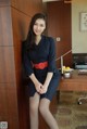 A woman in a black dress sitting on a desk.