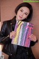 A woman in a black leather jacket holding up a colorful painting.