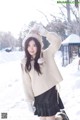 A woman in a white sweater and black skirt posing in the snow.