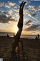 A woman doing a handstand on the beach at sunset.