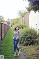 A woman in a plaid shirt and jeans standing on a path.