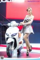 A woman standing next to a white scooter on display.