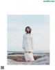 A woman in a white dress standing on a rock by the ocean.