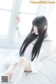 A woman in a white dress sitting on a bed.