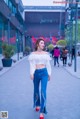 A woman in a white top and blue jeans is walking down the street.