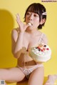 A woman in lingerie eating a cake on a yellow background.