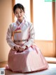 A woman in a pink and white hanbok sitting on the floor.