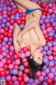 A woman laying in a ball pit of pink and purple balls.