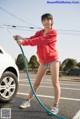 A young woman is washing her car with a hose.