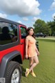 A woman standing next to a red jeep in a field.